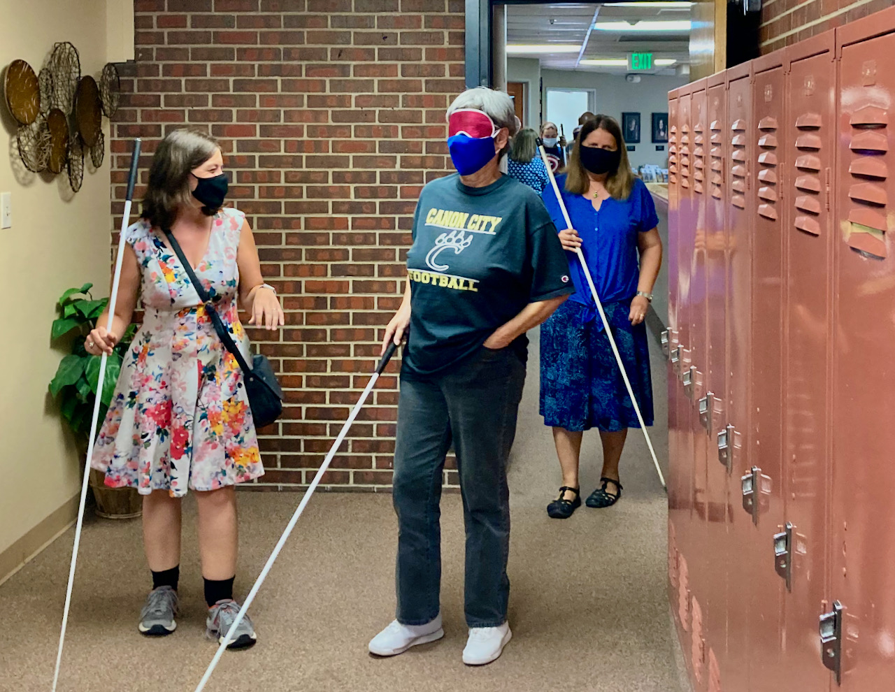 An Older Blind woman navigates the hallway among other students with her instructor following
