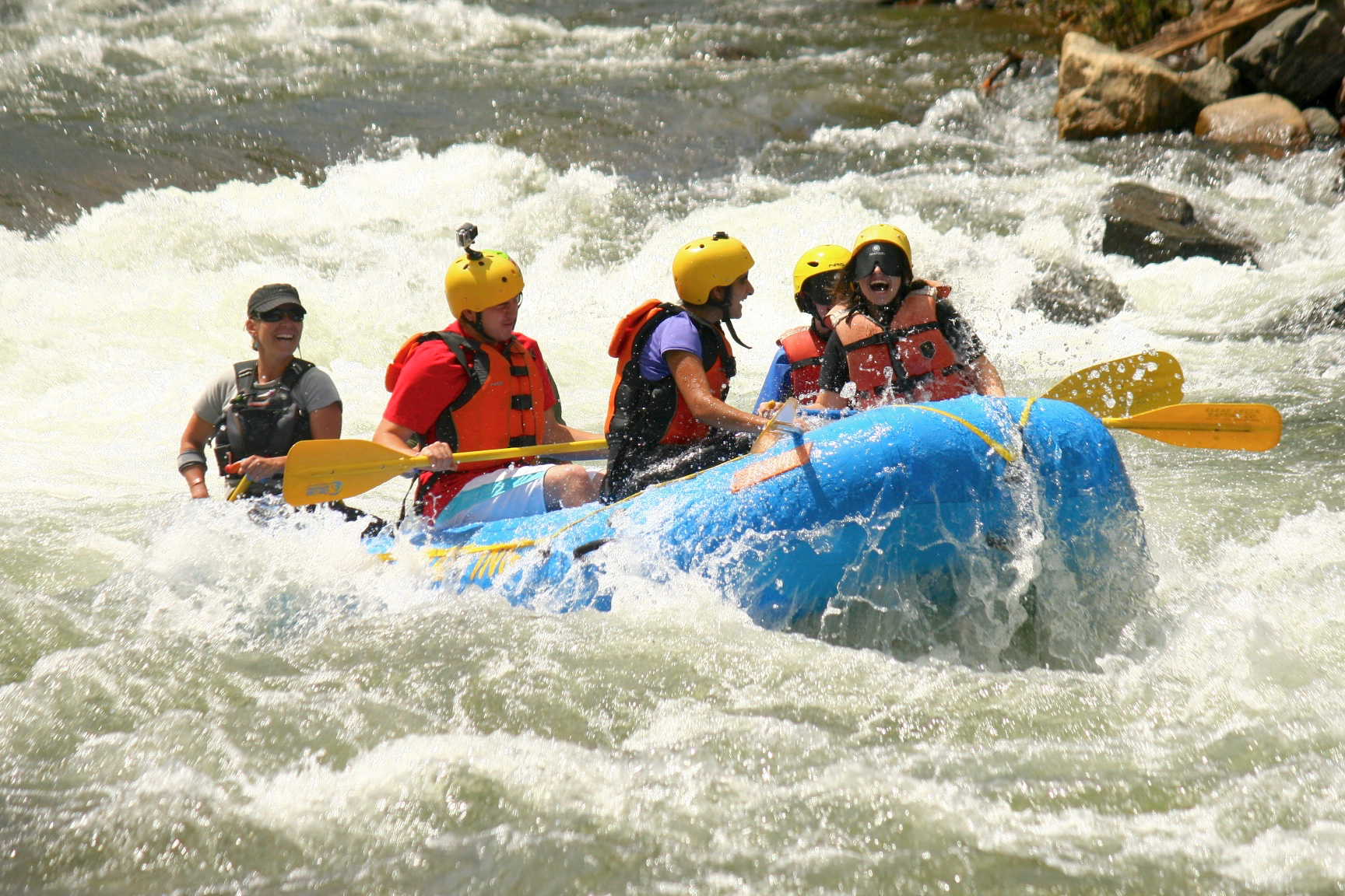 The front of the raft lifts up high as swirling white water splashes all around
