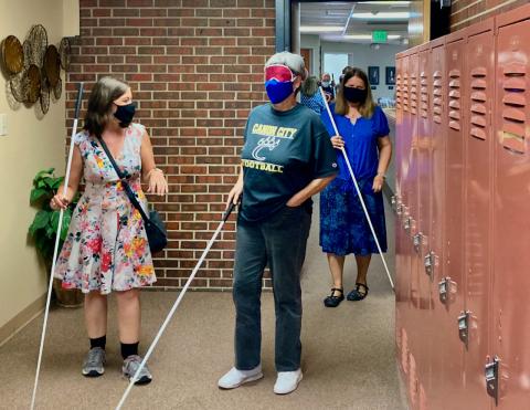 An Older Blind woman navigates the hallway among other students with her instructor following