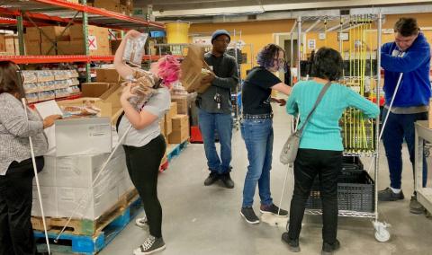 Five blind people unpack, carry and shelve food items along with a food bank staffer.