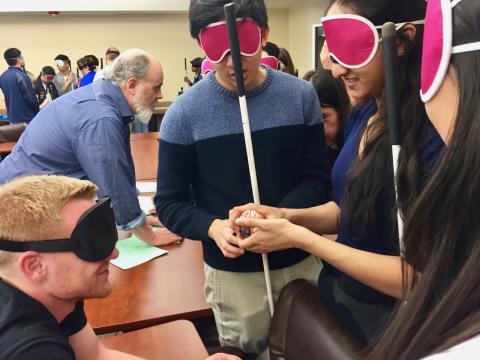 Ryan shows three Rice students a hands-on model of a brain while wearing sleepshades